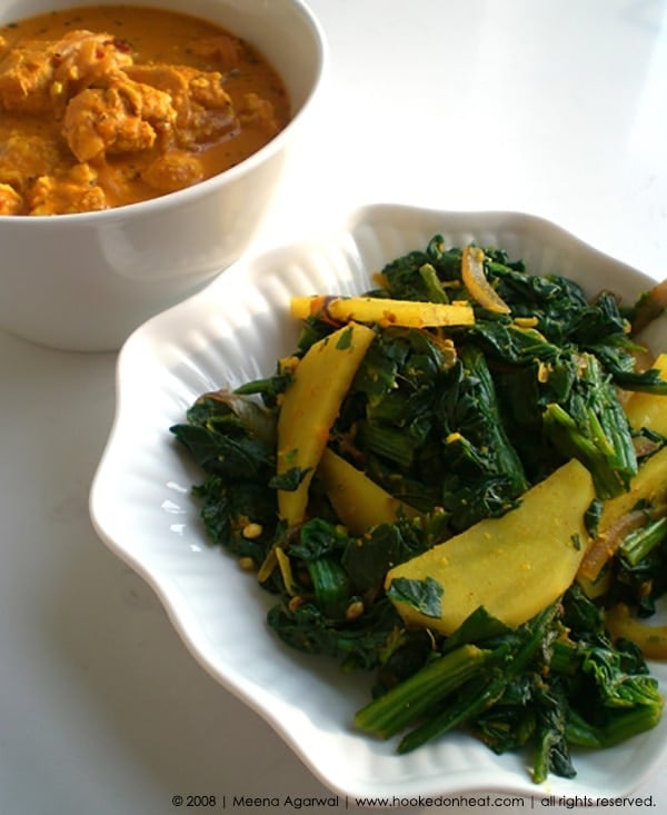 A bowl of Aloo Palak (Sauteed Spinach with Potatoes) served with a side of Chicken Curry.