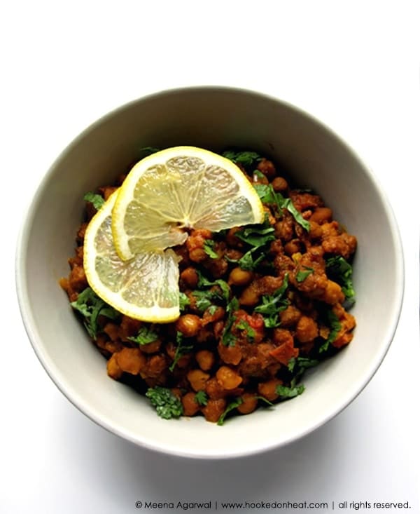 A bowl of Kala Chana Masala, also known as Sukhe Kale Chane, garnished with fresh cilantro and lemon wedges.