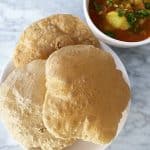 A plate of crispy Puris with a bowl of Aloo Bhaji on the side