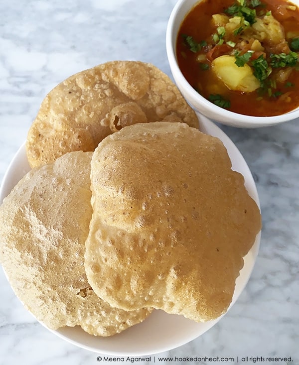 A plate of crispy Puris with a bowl of Aloo Bhaji on the side