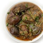 A bowl of Baingan Masala or Aubergine Curry garnished with fresh cilantro.