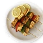 A platter of Paneer Tikka Shashlik skewered with onions and peppers.