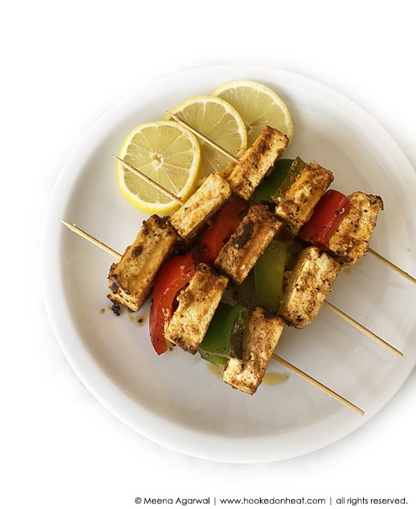 A platter of Paneer Tikka Shashlik skewered with onions and peppers.