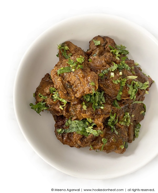 A bowl of Bhuna Chicken, also known as Chicken Bhuna Masala, garnished with fresh cilantro leaves.