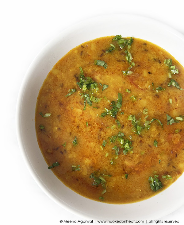A bowl of yellow arhar dal garnished with chopped fresh cilantro, set against a white background.