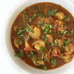 A white bowl filled with Indian shrimp curry in a rich, reddish-brown sauce, garnished with fresh chopped cilantro.