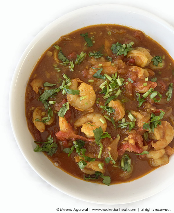 A white bowl filled with Indian shrimp curry in a rich, reddish-brown sauce, garnished with fresh chopped cilantro.